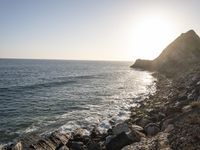 the sun setting over an island with waves coming up from it's shoreline