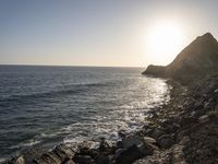 the sun setting over an island with waves coming up from it's shoreline