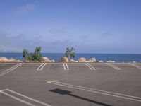 a parking lot that looks empty and empty in front of the ocean, next to some rocks