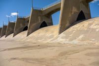 a close up of some concrete in the sand with water and a bridge in the background