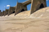 a close up of some concrete in the sand with water and a bridge in the background