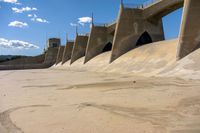 a close up of some concrete in the sand with water and a bridge in the background