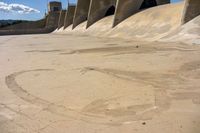 a close up of some concrete in the sand with water and a bridge in the background