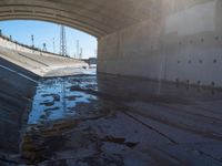 a picture of an empty tunnel underpass with water running below it and the sky is blue