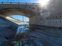 a picture of an empty tunnel underpass with water running below it and the sky is blue