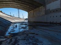 a picture of an empty tunnel underpass with water running below it and the sky is blue