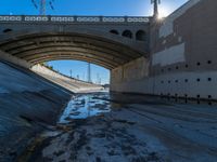 a picture of an empty tunnel underpass with water running below it and the sky is blue