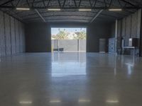 a concrete floor in a warehouse with two doors open to the side with a metal ceiling and lighting