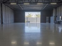 a concrete floor in a warehouse with two doors open to the side with a metal ceiling and lighting