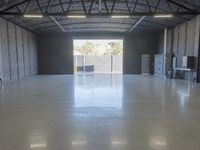 a concrete floor in a warehouse with two doors open to the side with a metal ceiling and lighting