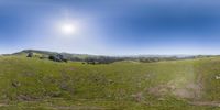 a 360 - degree lens image of hills with a field of grass on it, with the sun in the sky above them