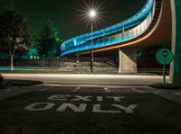 the curved bridge is lit up blue with green light on it's sides and is over a road in front of a concrete wall