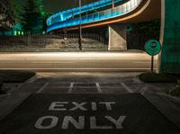 the curved bridge is lit up blue with green light on it's sides and is over a road in front of a concrete wall