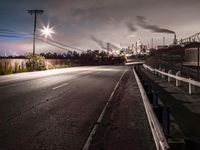 the city is covered with smoke and smokestacks behind a fence and the roadway