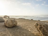 a beach scene with large rocks and the ocean in the background, near a city