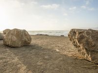 a beach scene with large rocks and the ocean in the background, near a city