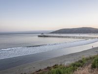 the ocean next to the pier and grassy area in the morning sun rises over the water