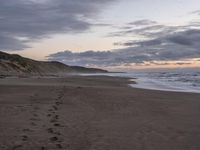 footprints are on the sandy beach next to the ocean with mountains in the background in the sunset