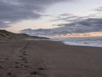 footprints are on the sandy beach next to the ocean with mountains in the background in the sunset