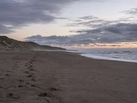 footprints are on the sandy beach next to the ocean with mountains in the background in the sunset