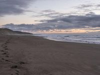 footprints are on the sandy beach next to the ocean with mountains in the background in the sunset