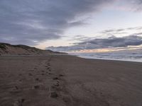 footprints are on the sandy beach next to the ocean with mountains in the background in the sunset