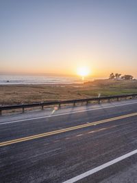 the sun is setting over the ocean, and it's setting over the road