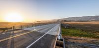 the sun rises over an empty highway by some mountains with a sign on it indicating the right curve