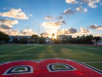 a photo of the sun shining in a cloudy sky at sunset on football field with a large d painted red