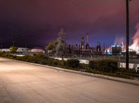 a street scene with cars, a factory and trees at night in the background with sky full of smoke