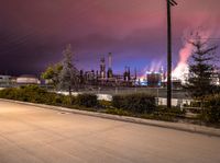 a street scene with cars, a factory and trees at night in the background with sky full of smoke