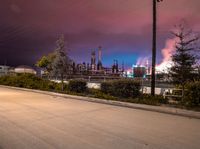 a street scene with cars, a factory and trees at night in the background with sky full of smoke