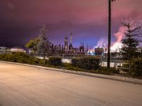 a street scene with cars, a factory and trees at night in the background with sky full of smoke