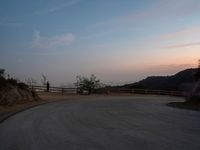 a person on a skateboard rides down the side of a mountain road at dusk