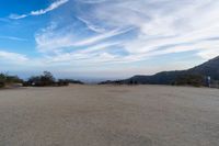 two women sit on a bench on top of a dirt field on a hillside overlooking the horizon