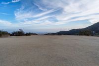 two women sit on a bench on top of a dirt field on a hillside overlooking the horizon