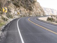 an empty highway with rocks and rock formations, yellow and white signs, and a curve of road