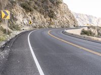 an empty highway with rocks and rock formations, yellow and white signs, and a curve of road