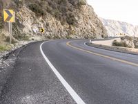 an empty highway with rocks and rock formations, yellow and white signs, and a curve of road