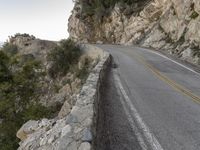 the road runs along a cliff and the car is parked in the street under it