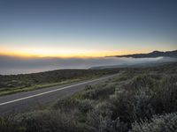 the sun is rising over the mountains above the road and the fog is on the horizon