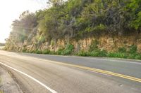 a long road with a rock cliff on the side, which has a yellow strip to show its colors