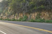 a long road with a rock cliff on the side, which has a yellow strip to show its colors