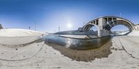 the fish - eye view of a boat out on the beach under a bridge on a sunny day