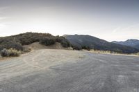 a motorcycle driving on an empty road near a mountain area as the sun goes down