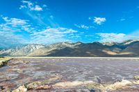 mountains covered with vegetation are near a large lake covered in water and some rocks on the bottom of a sandy flat land