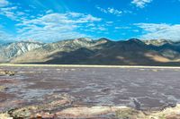 mountains covered with vegetation are near a large lake covered in water and some rocks on the bottom of a sandy flat land