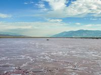 an open area with some water and some rocks near some mountains with a sky background