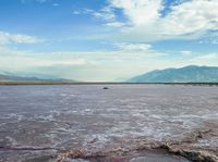 an open area with some water and some rocks near some mountains with a sky background