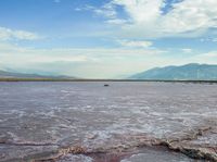 an open area with some water and some rocks near some mountains with a sky background